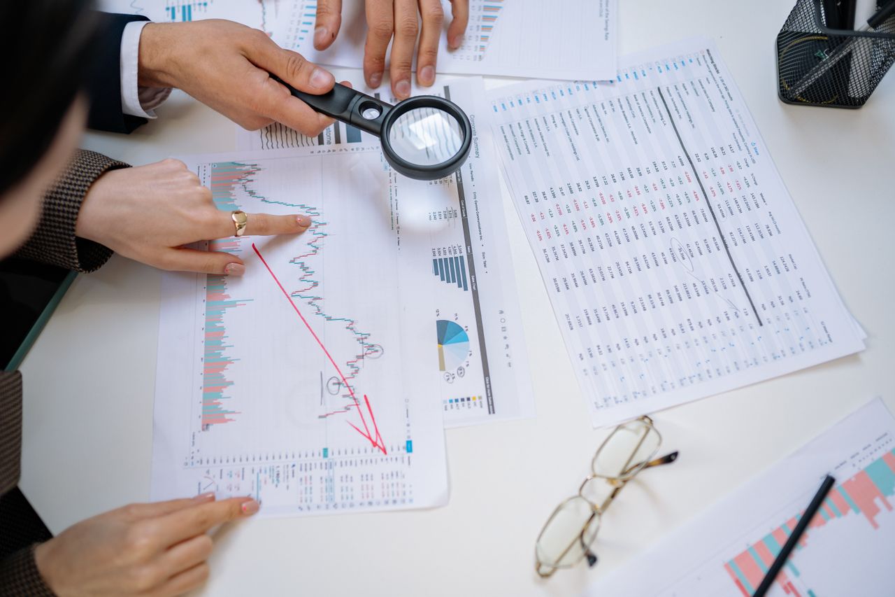 about-02 Business professionals examining financial documents with magnifying glass for detailed analysis.